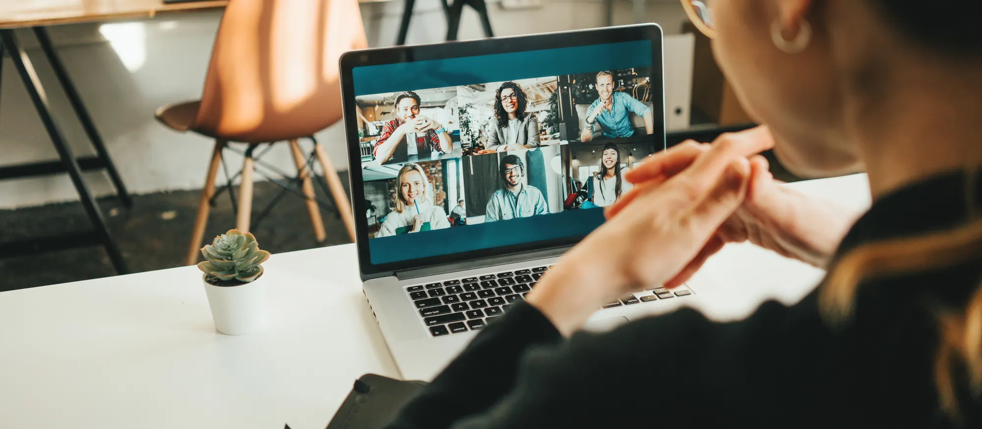 Iemand volgt een videovergadering op de laptop, aan een bureau met een plant